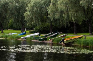 Several colorful boats are resting on the shore of a lake in a peaceful park. Kallavesi lake, Kuopio Finland clipart