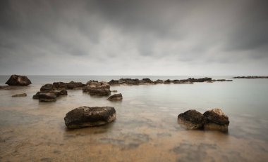 Turkuaz deniz suyu bulutlu bir günde sahildeki kayaların üzerinde yavaşça süzülüyor. Cape Greko yarımadası Kıbrıs