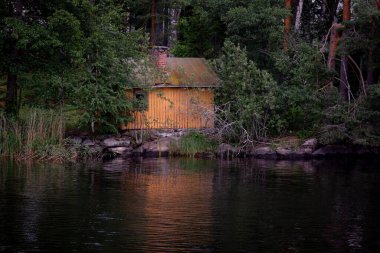Ormandaki küçük ahşap sauna evi gün batımında sakin göl suyuna yansıyor.