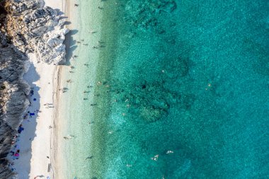 Tropik bir plajın berrak sularında yüzen turistlerin insansız hava görüntüsü.