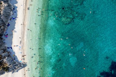 Turkuaz sular, turistlerin yaz aylarında güneşlendikleri ve yüzdükleri tenha bir plajda nazikçe tur atar. Tropik Kefalonya plajı Yunan adaları. Drone hava görüntüsü