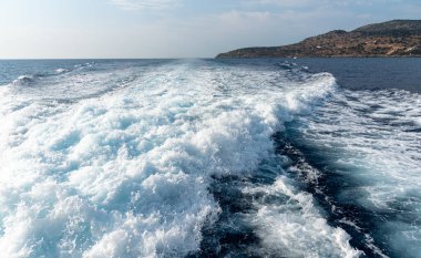 Beyaz köpük mavi denizde bir teknenin arkasında iz bırakıyor.
