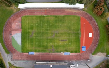 Birds eye drone view of an empty athletics track surrounding a green football field, ready for sporting events clipart