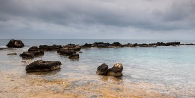 Turkuaz deniz suyu bulutlu bir günde sahildeki kayaların üzerinde yavaşça süzülüyor. Cape Greko yarımadası Kıbrıs