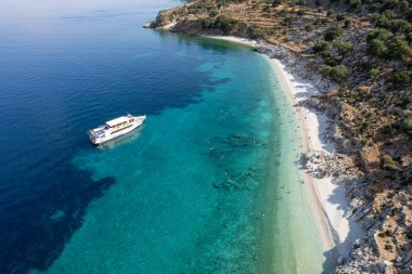 Turistlerin güneşli bir yaz gününün tadını çıkardıkları, turkuaz suyla ıssız bir Yunan plajının insansız hava aracı manzarası. Turist teknesi kıyıya demir attı. İyon Denizi 'ndeki Kefalonia Yunan adası