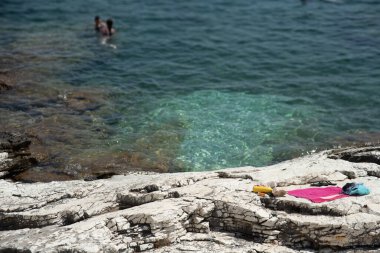 İnsanlar turkuaz suda yüzerken havlular, güneş kremi ve parmak arası terlikler güneşli bir sahilde beyaz kayaların üzerinde uzanıyordu. Kefalonya Yunanistan