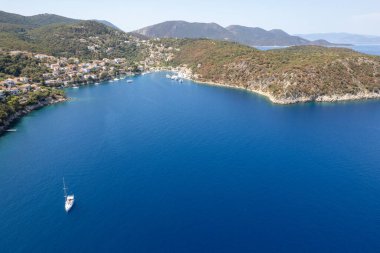 Yelkenli, derin mavi Ege Denizi 'nde bir Yunan adasında bir limanın yanında yelken açıyor.