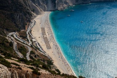 Tropical beach view with crystal clear water with tourist people on the shore. Myrtos famous beach ionian sea Kefalonia Greece. clipart