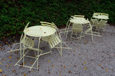 Sarı metalik bahçe sandalyeleri ve yuvarlak masalar sonbahar mevsiminde boş bir kahve dükkanında çakıl zemine istiflenmiş.