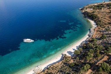 Turistlerin insansız hava aracı sahnesi, turkuaz suyla ıssız bir Yunan plajında güneşli bir yaz gününün tadını çıkarıyor. Turist teknesi kıyıya demir attı. İyon Denizi 'ndeki Kefalonia Yunan adası