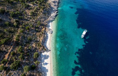 Turistlerin insansız hava aracı sahnesi, turkuaz suyla ıssız bir Yunan plajında güneşli bir yaz gününün tadını çıkarıyor. Turist teknesi kıyıya demir attı. İyon Denizi 'ndeki Kefalonia Yunan adası