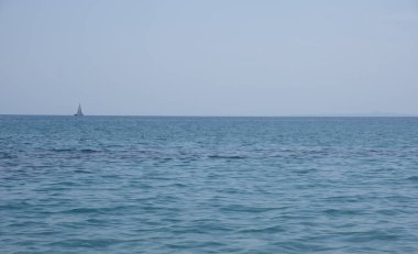 Yelkenli sakin mavi denizde yol alıyor. Arka planda berrak bir gökyüzü, huzurlu bir deniz manzarası.