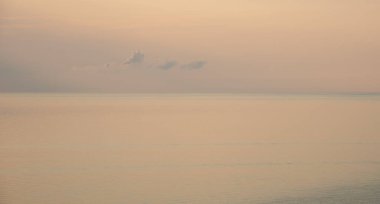 Minimalist deniz manzarası, günbatımında az bulutlu, pastel pembe gökyüzünü yansıtan sakin bir okyanus gösteriyor. Su üzerinde ufuk.