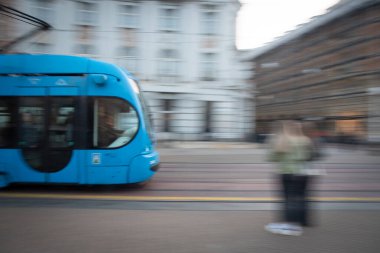 Şehir caddesinde bulanık bir insanın yanından geçen mavi tramvay. Toplu taşıma. Zagreb Hırvatistan