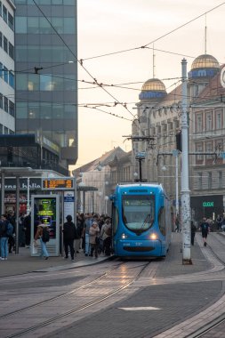 Zagrep, Coratia, 31 Ekim 2024: Bulutlu bir günde Hırvatistan 'ın zagreb kentindeki bir istasyonda modern bir tramvaya binen yolcular