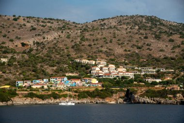 Hareketli tatil beldesi, sakin sularda demirli bir yelkenliyle bir Yunan adasının pitoresk kıyı şeridi boyunca uzanarak sakin bir tatil sahnesi oluşturuyor. Skala tatil beldesi, Kefonya Yunanistan