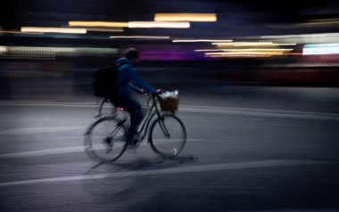 Tanınmayan kişi gece şehirde bisiklet sürüyor. Bulanık ışıklar hız ve hareket algısı. Sağlıklı bir yaşam tarzı. Açık havada aktif insanlar