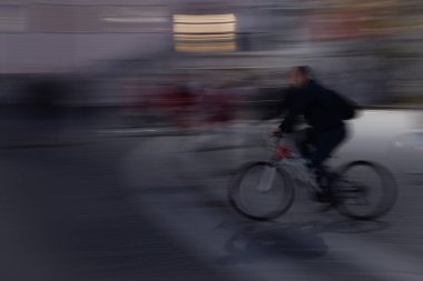 Geceleri şehirde bisiklet süren genç bir kadın bulanık ışıklarla hız ve hareket hissi yaratıyor.