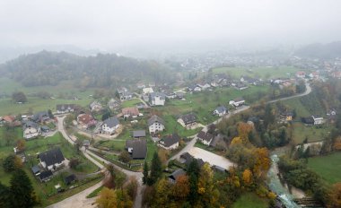 Slovenya 'nın Podhom köyü Radovna Vadisi' ndeki renkli sonbahar ağaçları ve sislerle çevrili nehir kenarındaki evlerin insansız hava aracı görüntüsü