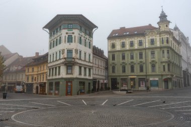 Ljubljana, Slovenia, October 30 2024: Cobblestone square with colorful buildings in slovenska bistrica, slovenia, on a foggy morning clipart