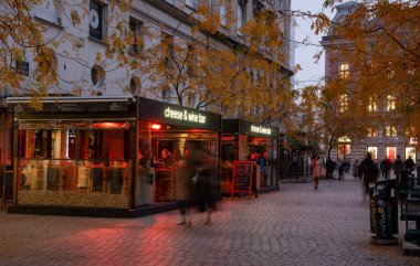 Zagreb, Hırvatistan, 31 Ekim 2024: Zagreb 'in Trg Avrupa Meydanı' nda akşam karanlığında bir restoran ve kaldırım taşı caddesindeki dükkanların yakınında yürüyen alışveriş ve banliyö sakinleri