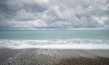 Okyanus dalgaları dramatik, bulutlu bir gökyüzünün altında kıyıya vuruyor, güzel ve huzurlu bir doğal manzara yaratıyor.
