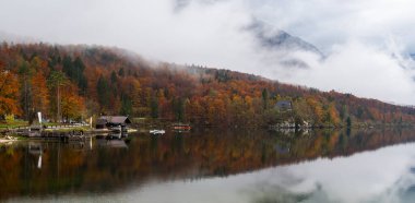 Bohinj Gölü 'nü çevreleyen alçak bulutlar durgun suya yansıyan renkli sonbahar yapraklarıyla kaplı.