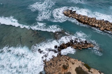 Turkuaz Akdeniz dalgaları kayalık bir kıyı şeridine çarpıyor ve dalgalar beyaz köpük ve hava manzarası yaratıyor.
