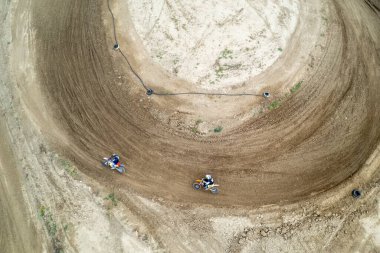 Yarış sırasında motosikletlerini toprak yolda süren iki motorsikletlinin hava görüntüsü.