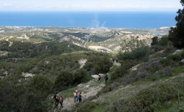 Bir grup turist yokuş aşağı yürüyüp Akdeniz kıyı şeridinin panoramik manzarasının tadını çıkarıyorlar. Kerynia İlçe Doğa Yolu