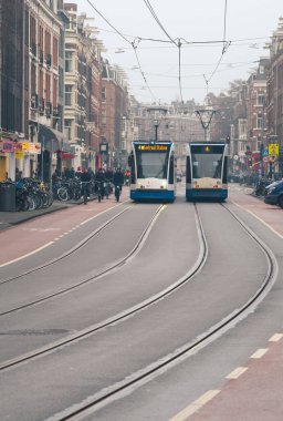 Amsterdam Hollanda, 9 Şubat 2025: Sisli bir günde Amsterdam şehir merkezindeki merkez istasyona doğru giden iki modern tramvay