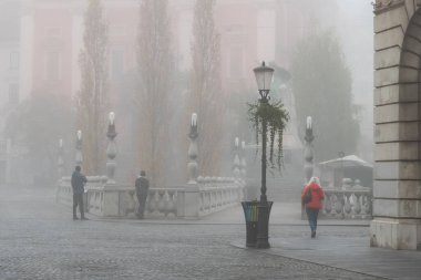 Avrupai bir şehirde sisli bir sabahta yürüyen vatandaşlar bir sokak lambası, balyalar ve taş bir köprü, ljubljana, Slovenya