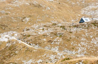 Dağda yürüyen yürüyüşçüler kuru otların arasında bir sığınağa gidiyor. Mountain Mangart Slovenya