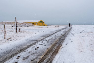 Karlı donmuş bir yol ve kışın İzlanda 'da bir tatil evine yürüyen tanınmamış bir adam. Fırtınalı hava