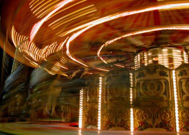 Dönen bir atlıkarıncanın parlak çizgileri, panayırdaki bir gecenin enerjisini ve heyecanını yakalıyor.