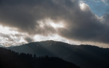 Fırtınalı bulutlu gün batımı ve dağ zirvesinin tepesinde parlak güneş ışınları. Kıbrıs Troodos Dağları