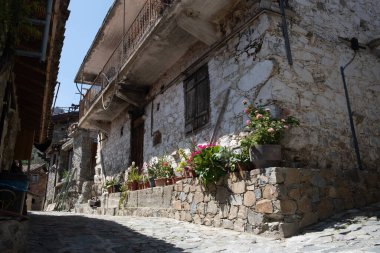 Çiçekler, Askas köyünün dar bir kaldırım taşı sokağındaki geleneksel evlerin taş cephelerini süslüyor.