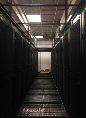 Metal ızgara zemin ve sunucu dolaplarının yer aldığı karanlık sunucu odası koridoru, veri merkezi altyapısını vurguluyor