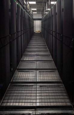 Metal ızgara zemin ve sunucu dolaplarının yer aldığı karanlık sunucu odası koridoru, veri merkezi altyapısını vurguluyor