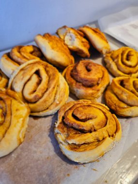 Parşömen kağıdında altın, yumuşacık tarçınlı rulo, tadını çıkarmaya hazır. Tatlı aromaları, pişirdikten sonra serinlerken rahat mutfağı doldurur..