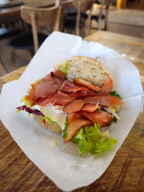 Tütsülenmiş somon sandviçi, kıtır marul, canlı sebzeler ve güzelce düzenlenmiş balıklar içeren ahşap bir masada oturur..
