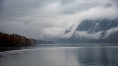 Bohinj Gölü 'nden sis yükseliyor ve arka plandaki dağları kaplıyor. Sonbahar mevsiminde gizemli bir atmosfer yaratıyor.