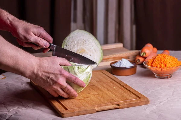 Cabbage on a cutting board, knife and carrot next to it.