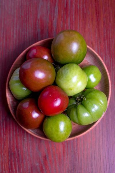 Green, red fresh tomatoes in wood bowl on the red table.