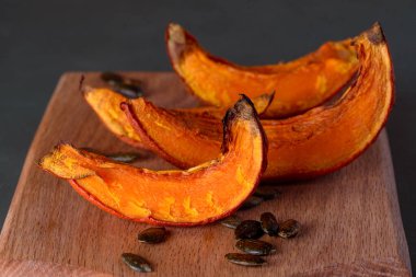 baked pumpkin. fried pumpkin slices on wood cutting board.