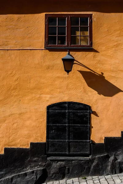 A wall street lamp on a residential building with yellow walls in sunshine. Black old metal door.
