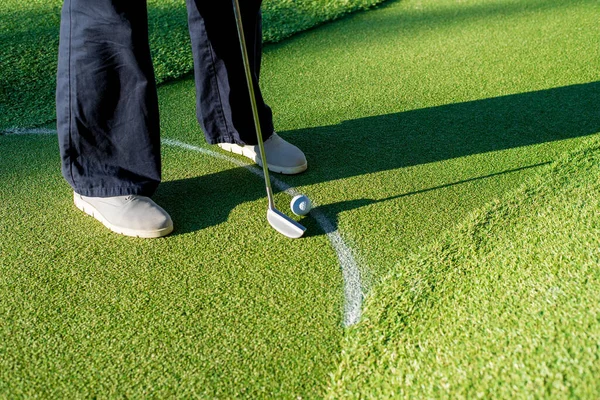 穿着灰色运动鞋的迷你高尔夫选手在绿道上的球洞里打高尔夫球 — 图库照片