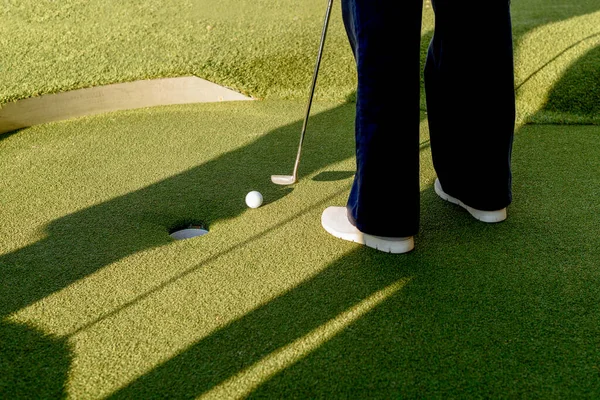 穿着灰色运动鞋的迷你高尔夫选手在绿道上的球洞里打高尔夫球 — 图库照片#