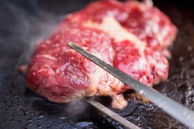 Şef ızgarada biftek pişiriyor. Izgaradan duman çıkıyor..