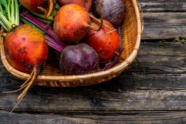 Tahta arka planda hasır sepetin içinde pancar kökleri. Olgun sarı, turuncu ve mor pancarlar..